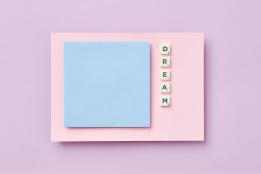 Flat lay of Scrabble tiles spelling 'dream' on pastel surroundings with copy space.