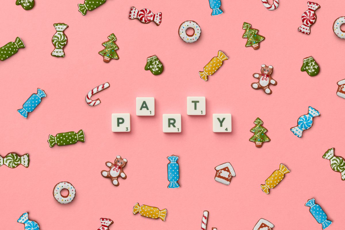 Colorful candies and cookie decorations arranged with party text on pink backdrop.