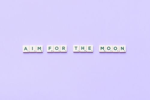 Free Scrabble tiles forming 'Aim for the Moon' on a purple background inspire motivation. Stock Photo