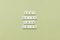 Scrabble tiles spelling 'Don't Raise Your Voice' on a green background.