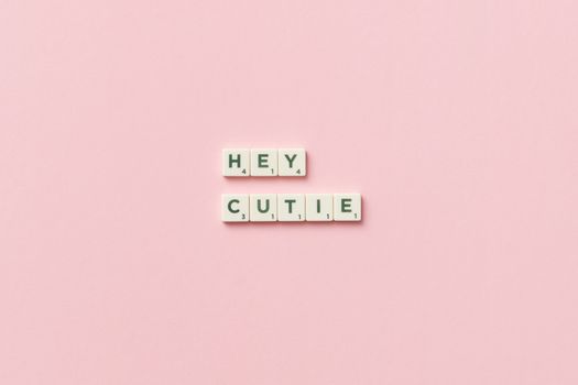Scrabble tiles spelling 'HEY CUTIE' on a pink background in a minimalist style.