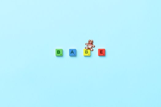 Scrabble letters spelling "BABE" with teddy bear on pastel blue surface, playful and colorful.