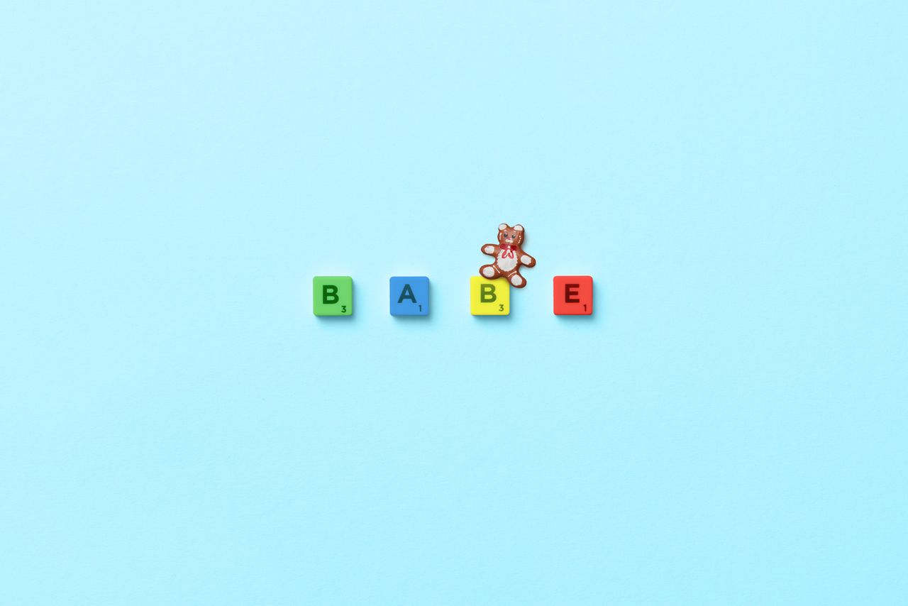 scrabble letters spelling babe with teddy bear on pastel blue surface