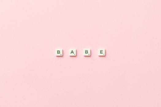 Scrabble tiles spelling 'Babe' placed on a soft pink background, top view.