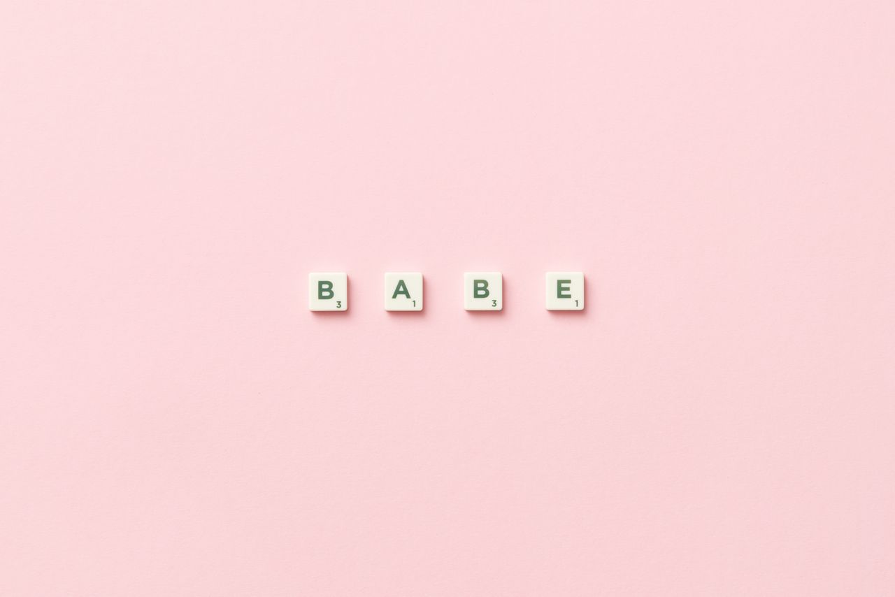 scrabble tiles spelling babe placed on a soft pink background top view