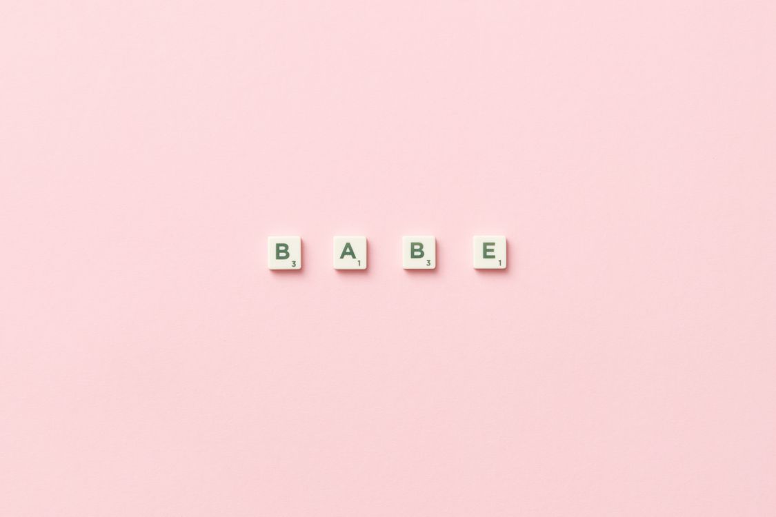 Free Scrabble tiles spelling 'Babe' placed on a soft pink background, top view. Stock Photo