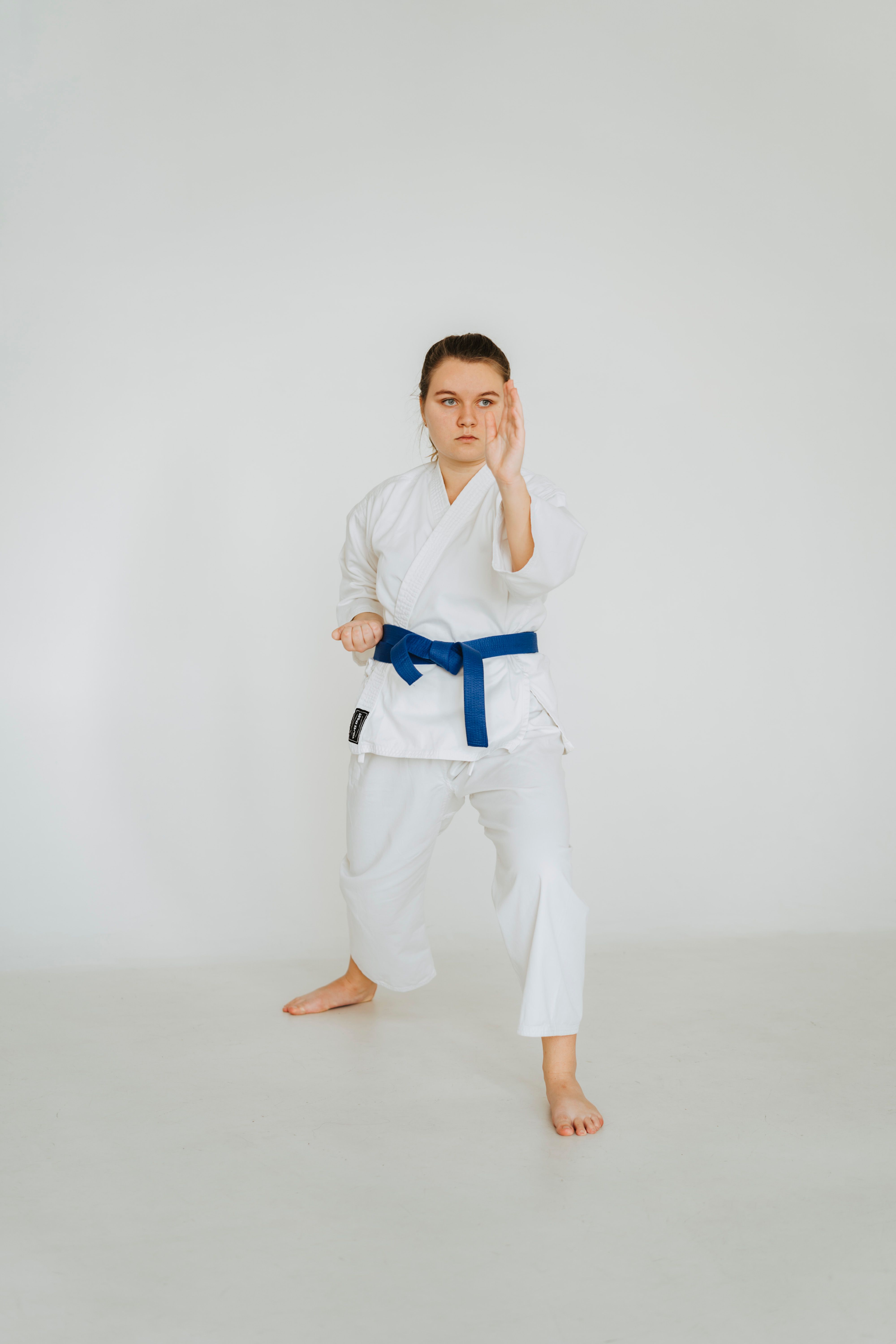 A woman martial artist in karate attire poses with a focused stance in a bright studio setting.