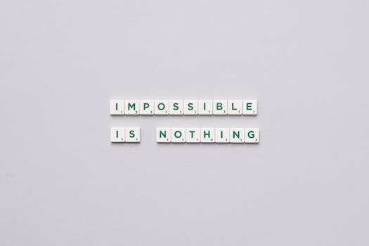 Flat lay of Scrabble tiles spelling 'Impossible is Nothing' on a neutral background.