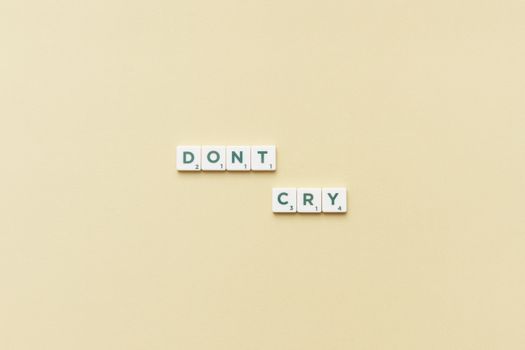 Scrabble tiles forming the phrase 'Don't Cry' on a simple yellow background, top view.