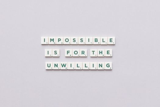 Inspirational quote 'Impossible is for the unwilling' made with letter tiles on a minimalist background.