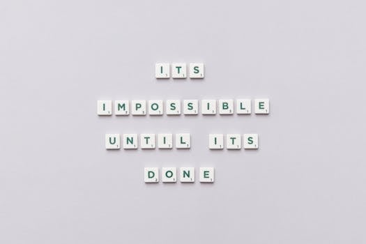 Motivational phrase 'It's impossible until it's done' arranged with Scrabble tiles on a gray background.