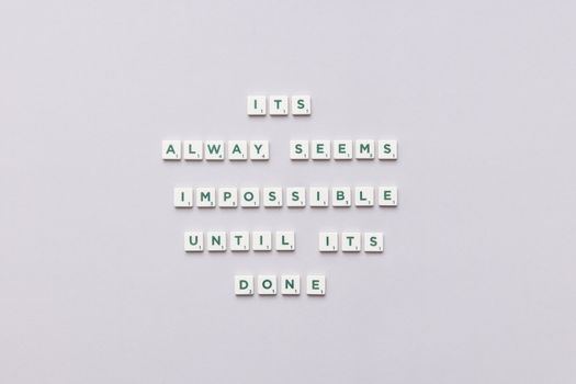 Motivational quote 'It always seems impossible until it's done' in Scrabble tiles.