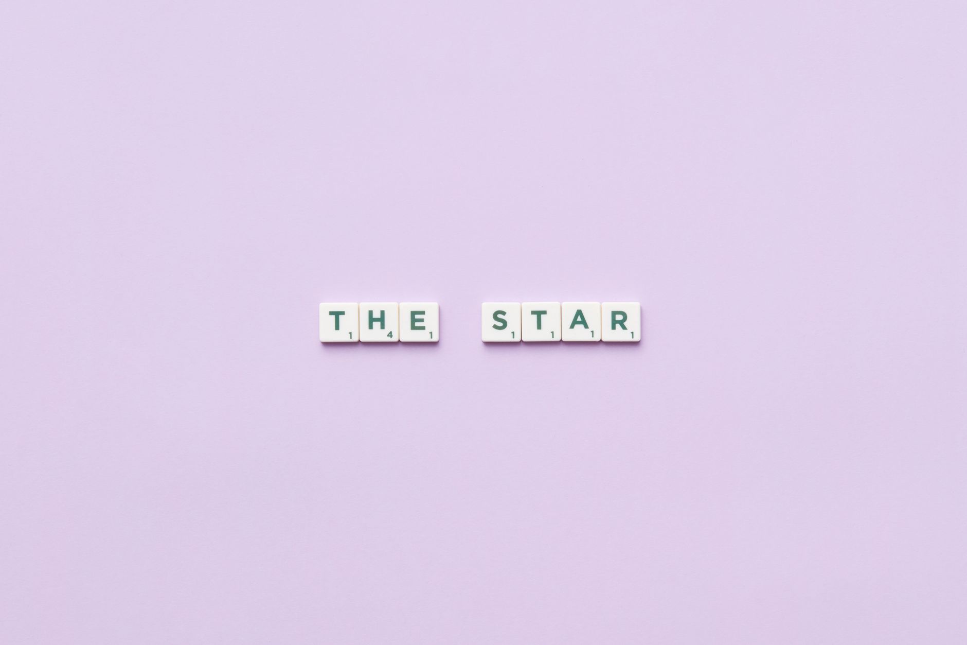 Scrabble tiles spelling 'The Star' on a soft pastel background, providing clean copy space.
