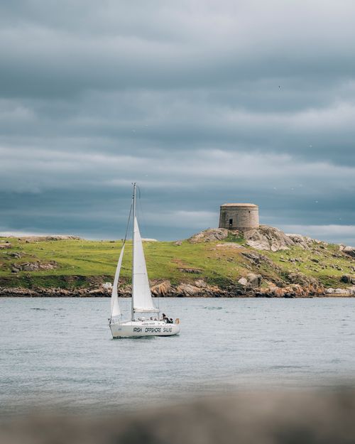 Free Scenic view of a sailboat near a historic Martello Tower in Dublin Bay, Ireland, under a cloudy sky. Stock Photo