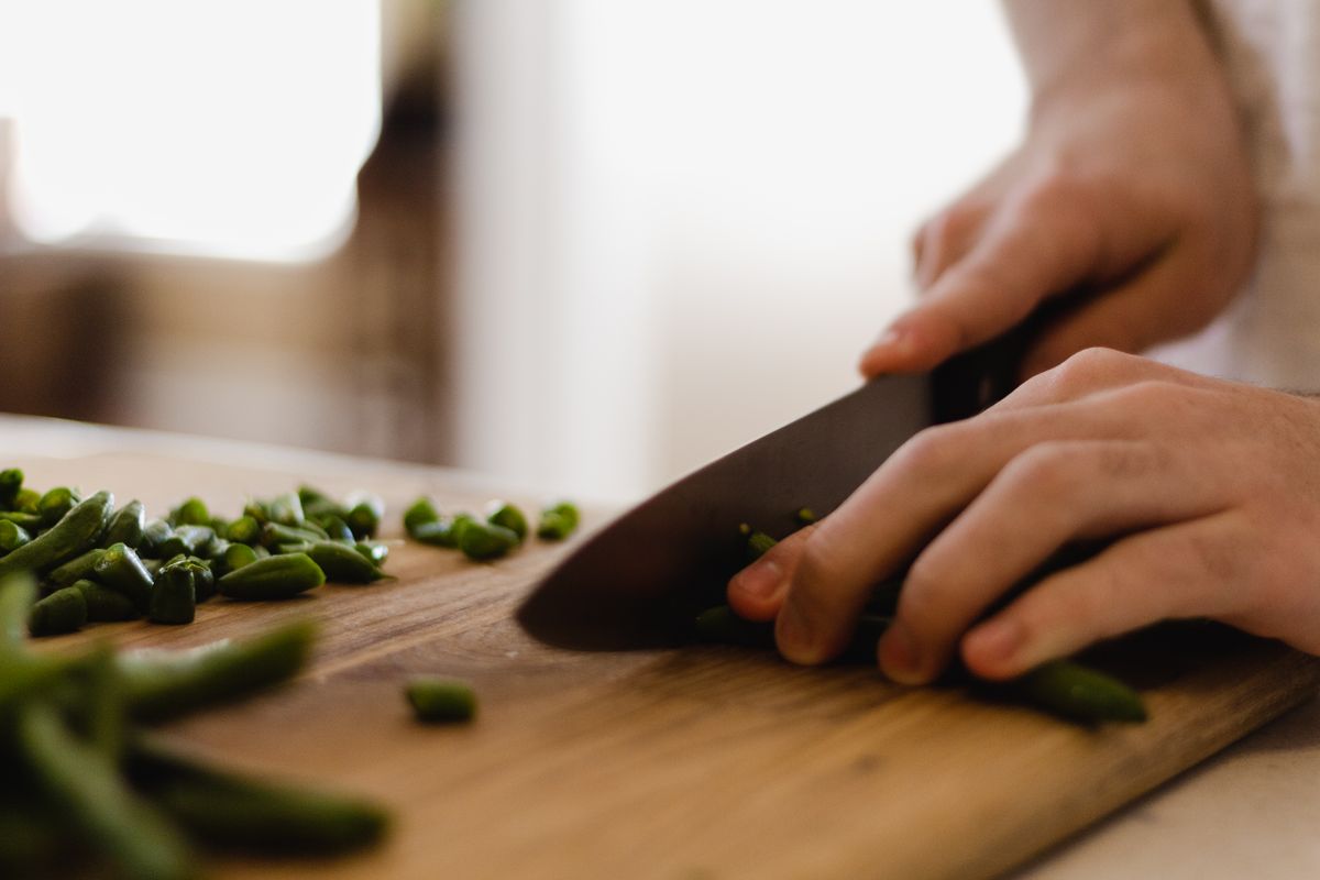 A person slicing fresh green beans with a knife on a cutting board — photo by Christianna Otto on Pexels