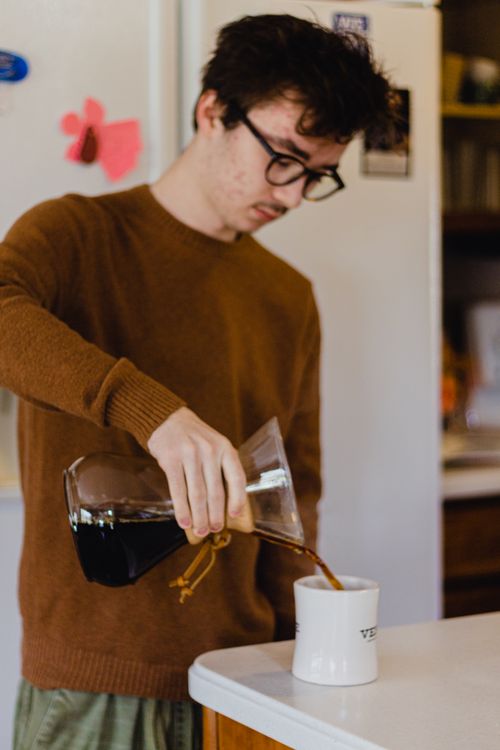 Free Casual portrait of a young man pouring fresh coffee into a mug in his kitchen. Stock Photo