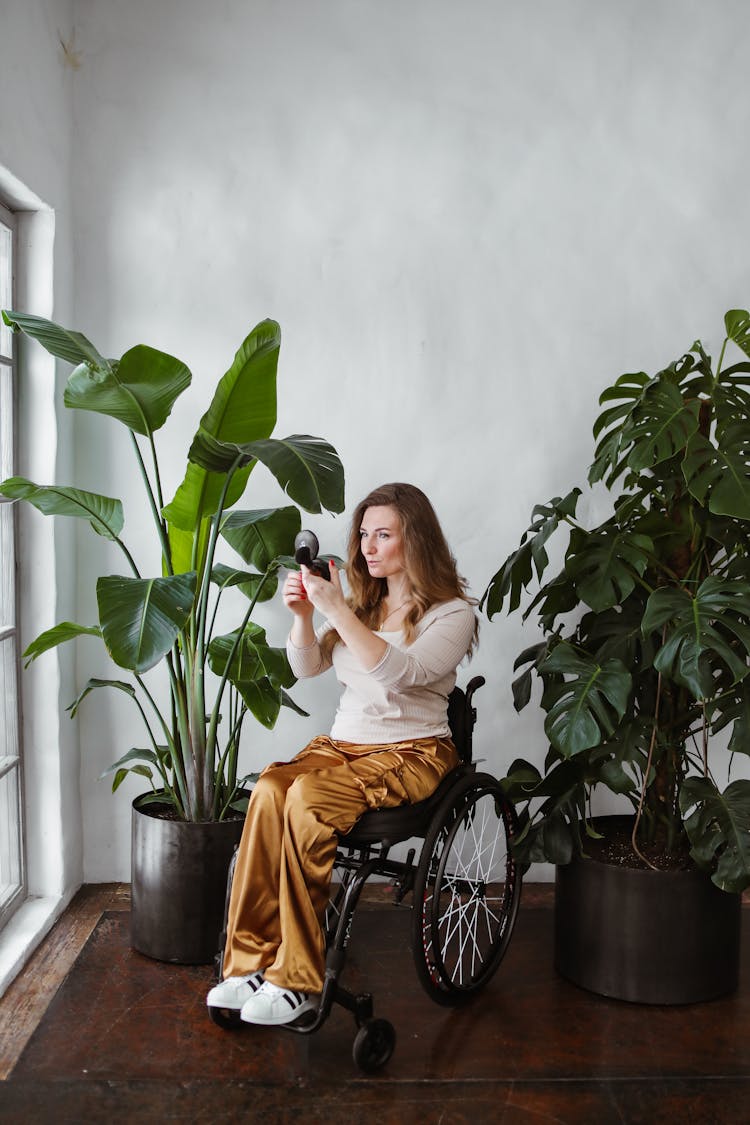 A Woman Sitting On The Wheelchair While Looking At The Compact Mirror