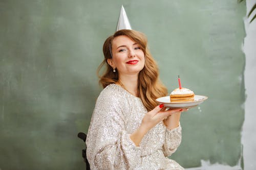 A Woman in Silver Dress Smiling while Holding a Plate with Sliced Cake