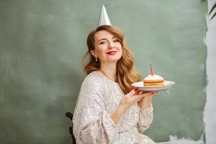 A Woman In Silver Dress Smiling While Holding A Plate With Sliced Cake