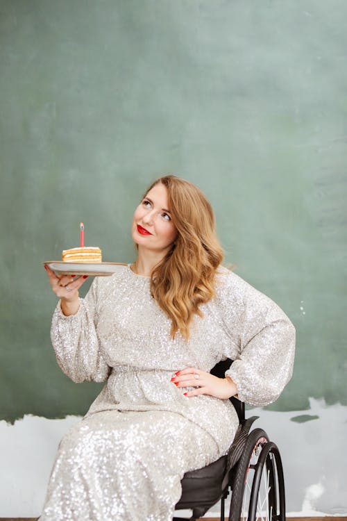 A Woman in Silver Dress Sitting on the Wheelchair while Holding a Plate with Cake