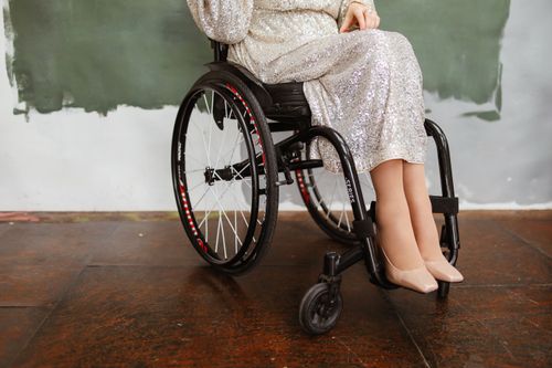 Free Woman in a silver sequin dress sitting in a wheelchair wearing beige heels, indoors. Stock Photo