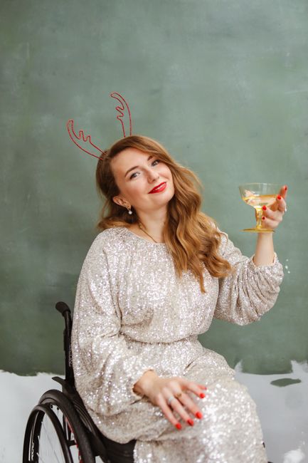 Happy woman in sequined dress celebrating New Year with wine, sitting in wheelchair.
