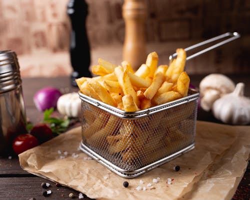 Free Composition of appetizing fresh french fries in steel basket placed on table amidst garlic and mushrooms Stock Photo