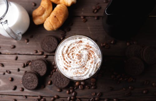 Whipped cream drink on table amidst coffee beans and cookies