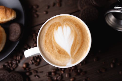 Top view composition of freshly brewed cappuccino served on dark table and surrounded by coffee beans and chocolate cookies