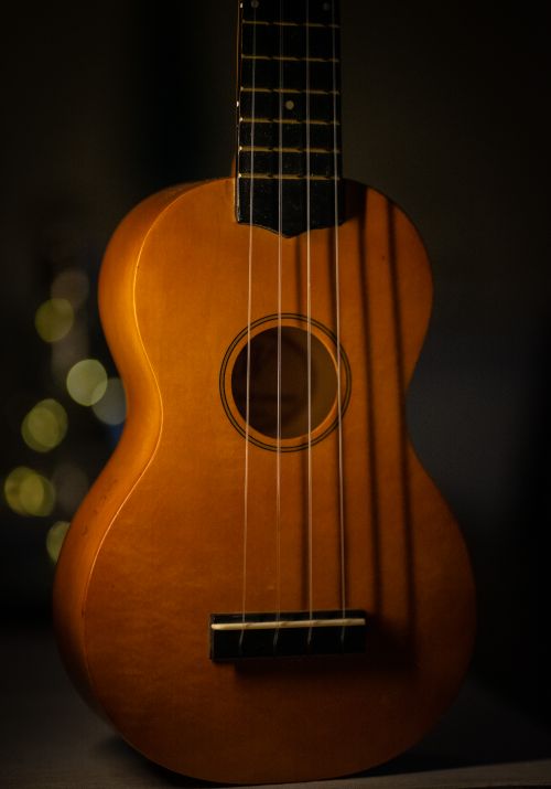 Free Minimalist close-up of a wooden ukulele with strings and dark background, showcasing acoustic design. Stock Photo