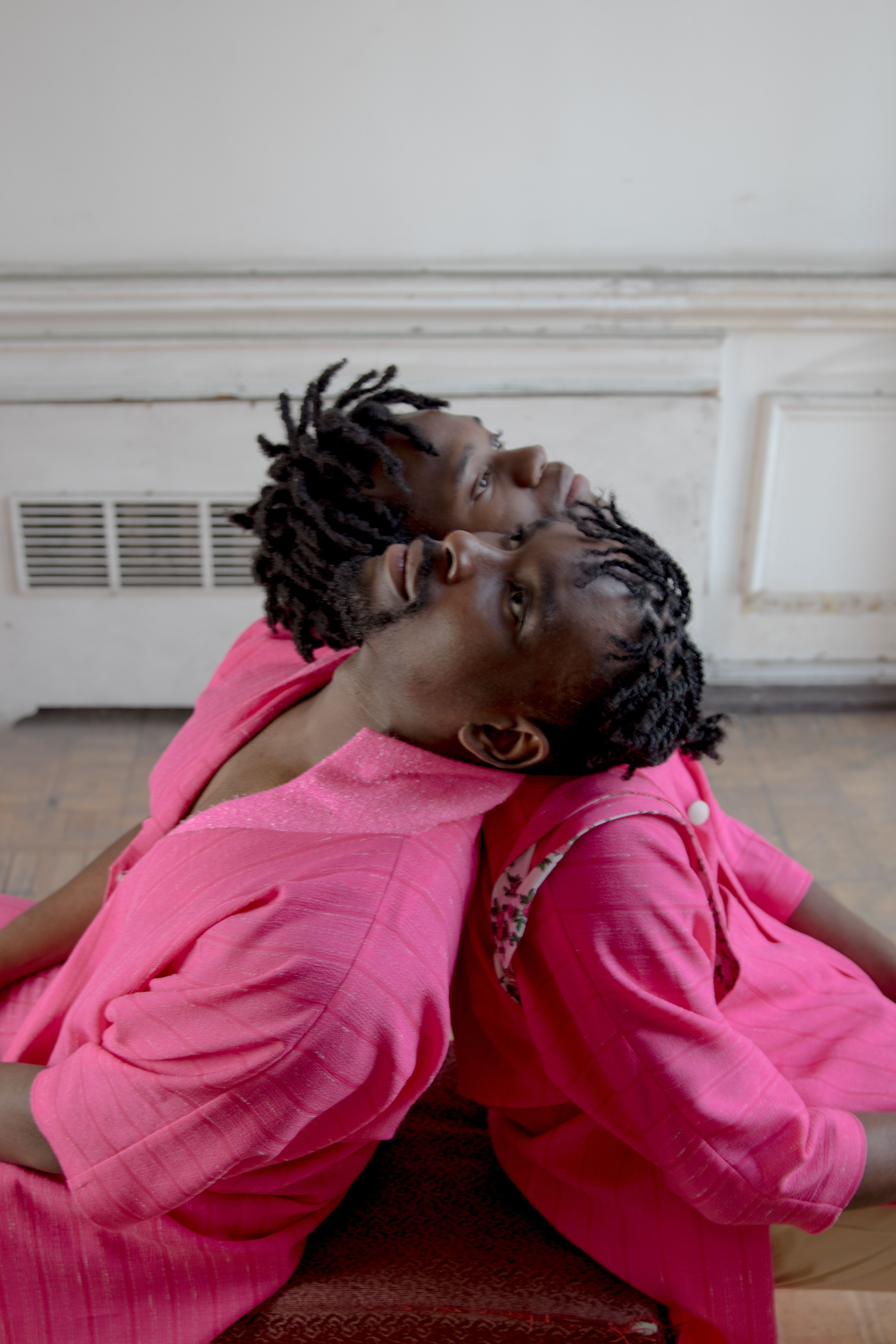 Artistic portrait of two adults in vibrant pink clothing, leaning back indoors.