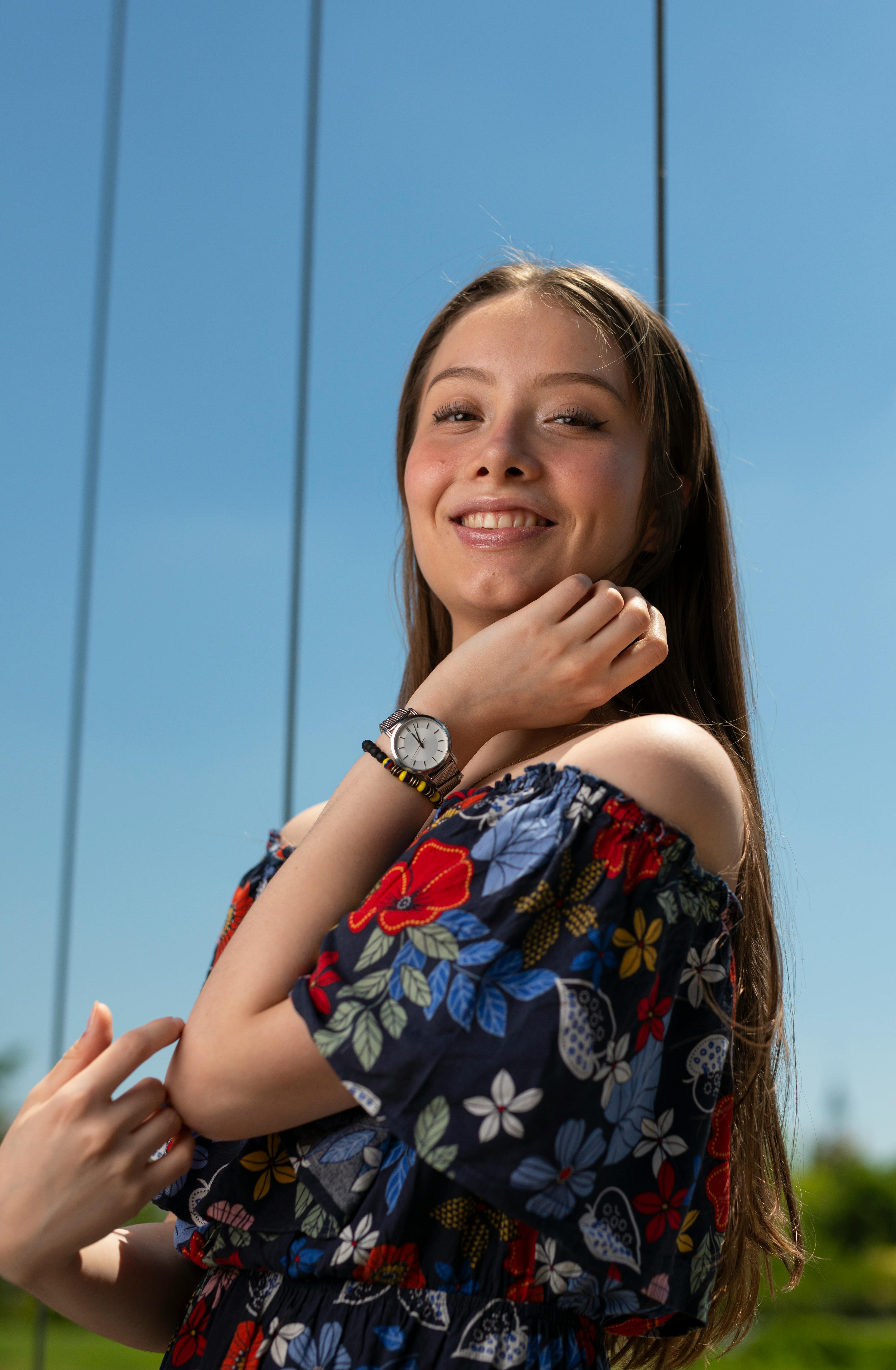 Smiling young woman in a floral off-shoulder dress enjoying a sunny day with a clear blue sky.