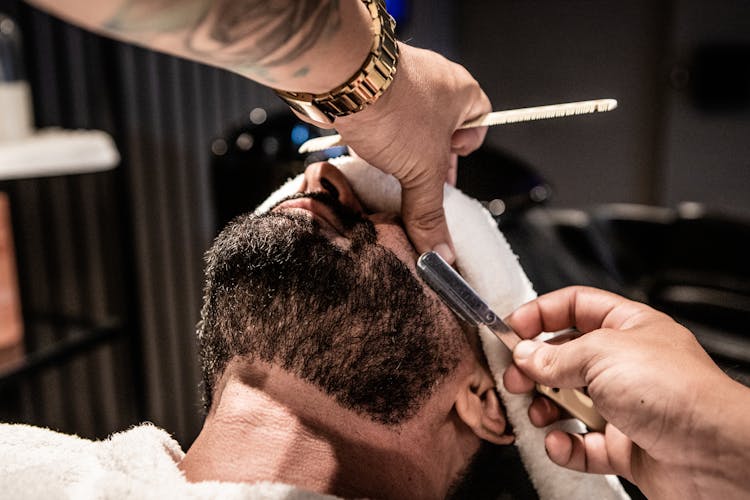 A Person Grooming A Man's Beard With A Razor