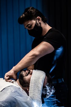 A barber expertly trims a client's beard in a stylish indoor setting in João Pessoa.