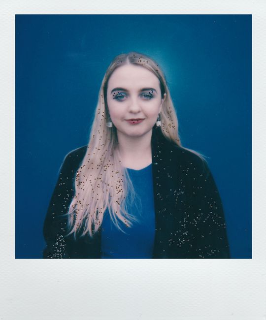 Fashionable portrait of a young blonde woman against a glittery blue backdrop.