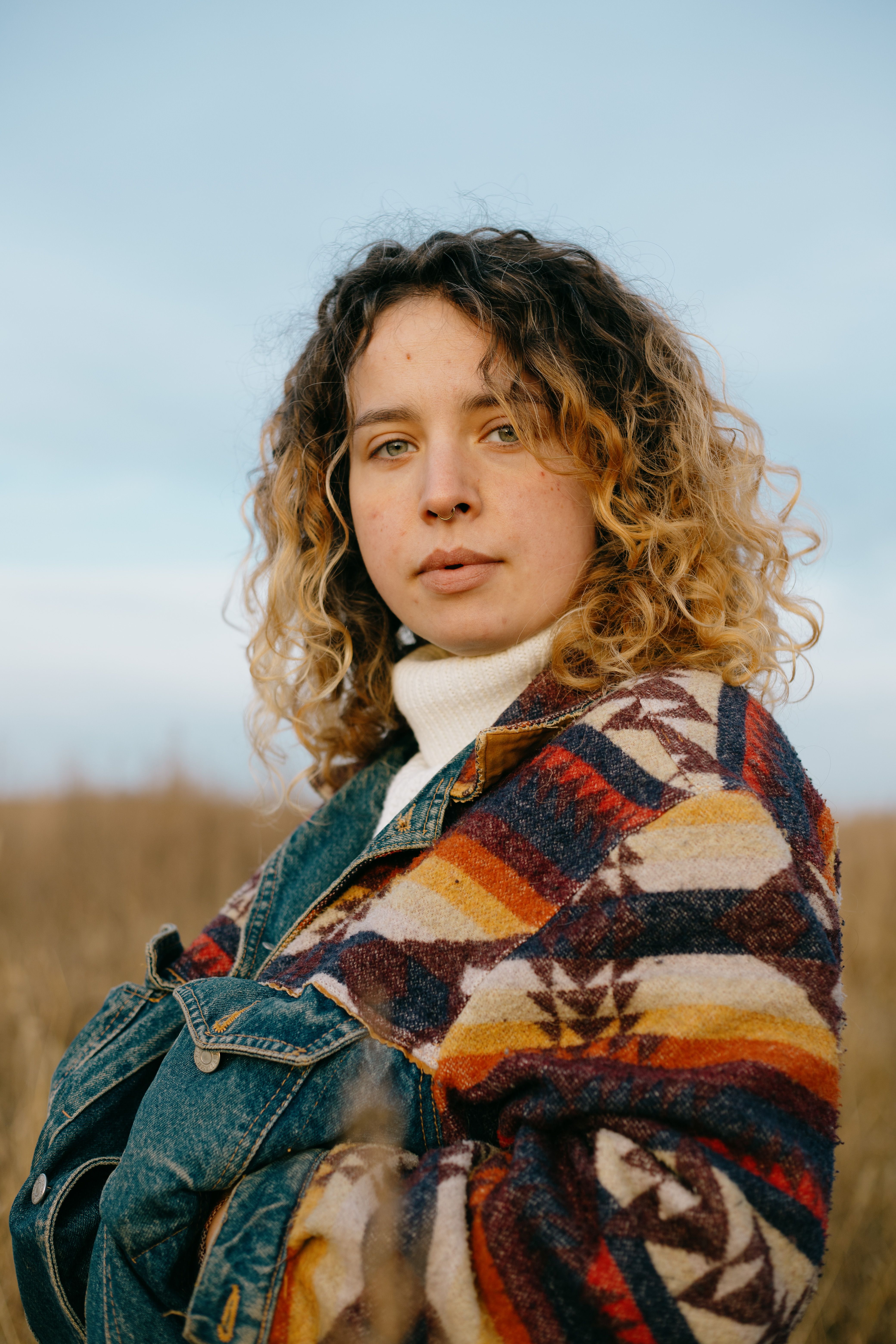 Close-up portrait of a woman with curly hair wearing a colorful blanket in a natural setting.
