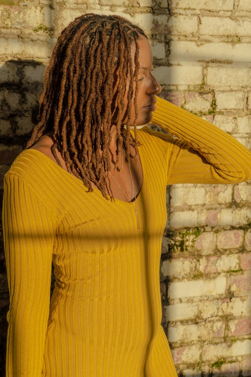 A Woman in Knitted Sweater Standing Near the Brick Wall