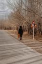 Woman with old heavy suitcase walking near asphalt road
