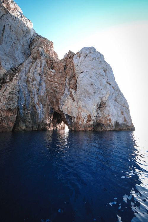 Free Rocky rough uneven formation with steep slope washed by rippling blue seawater in sunlight Stock Photo
