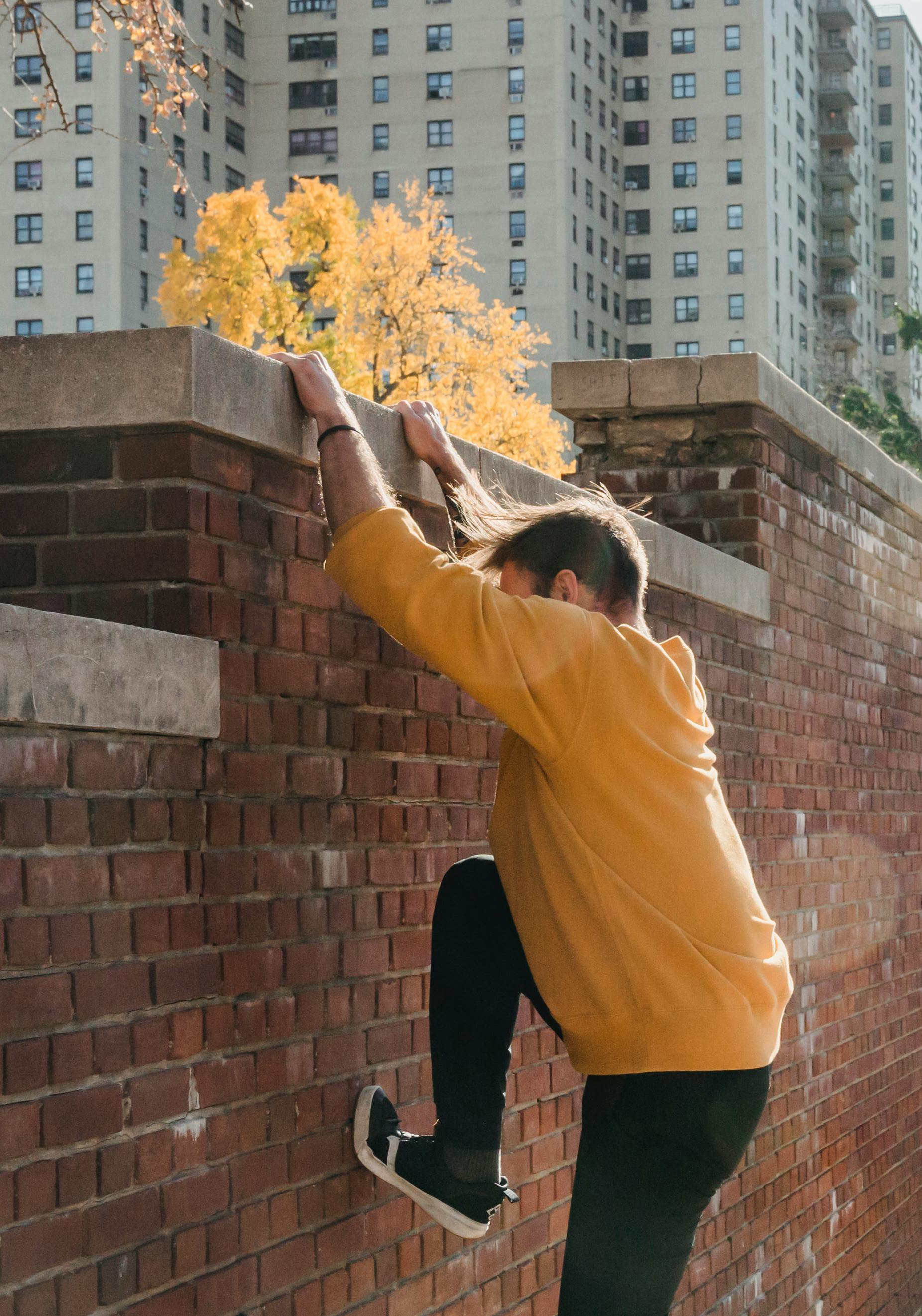 faceless male tracer climbing brick fence in park