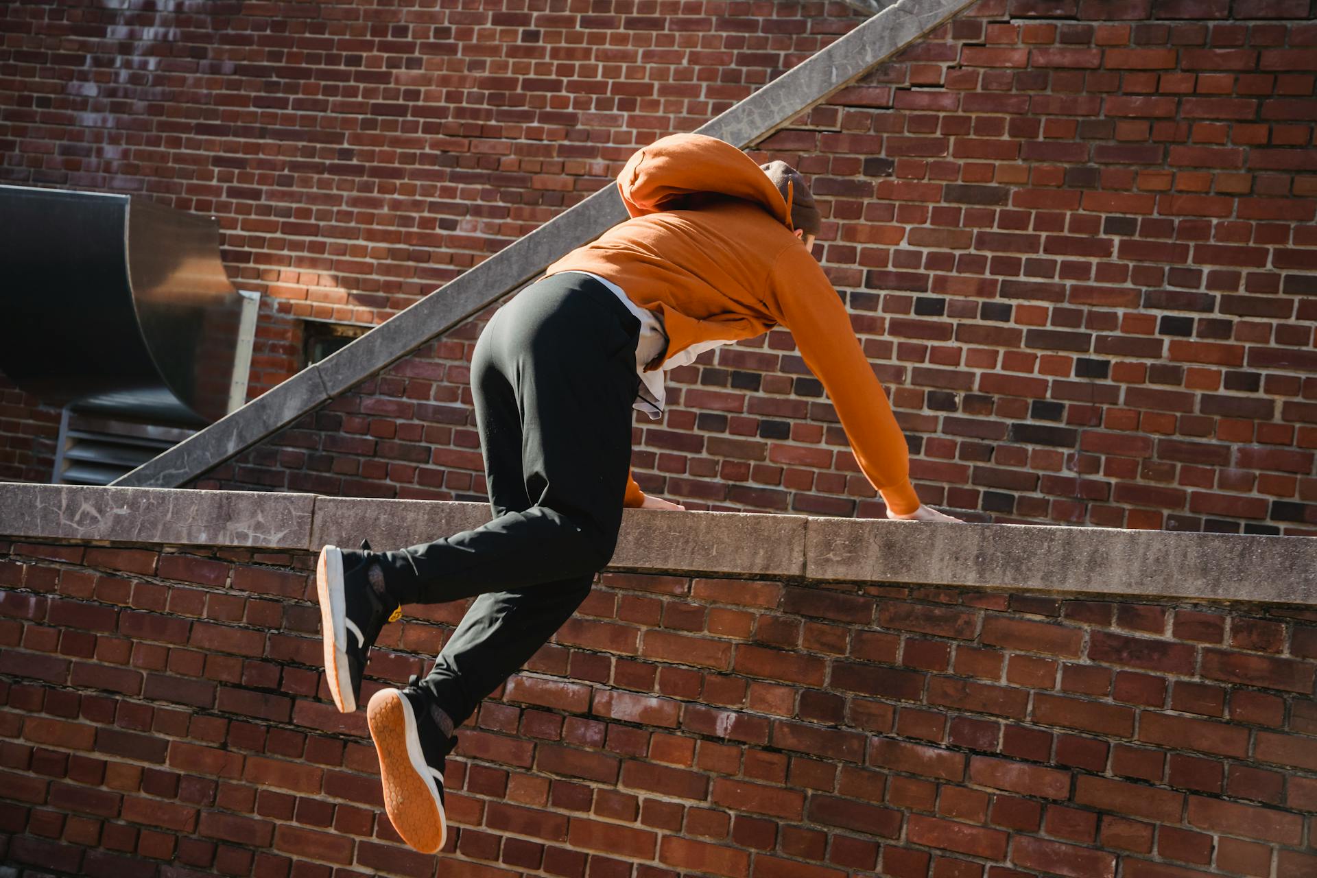Back view anonymous male tracer in casual wear performing tricks while practicing parkour on brick building