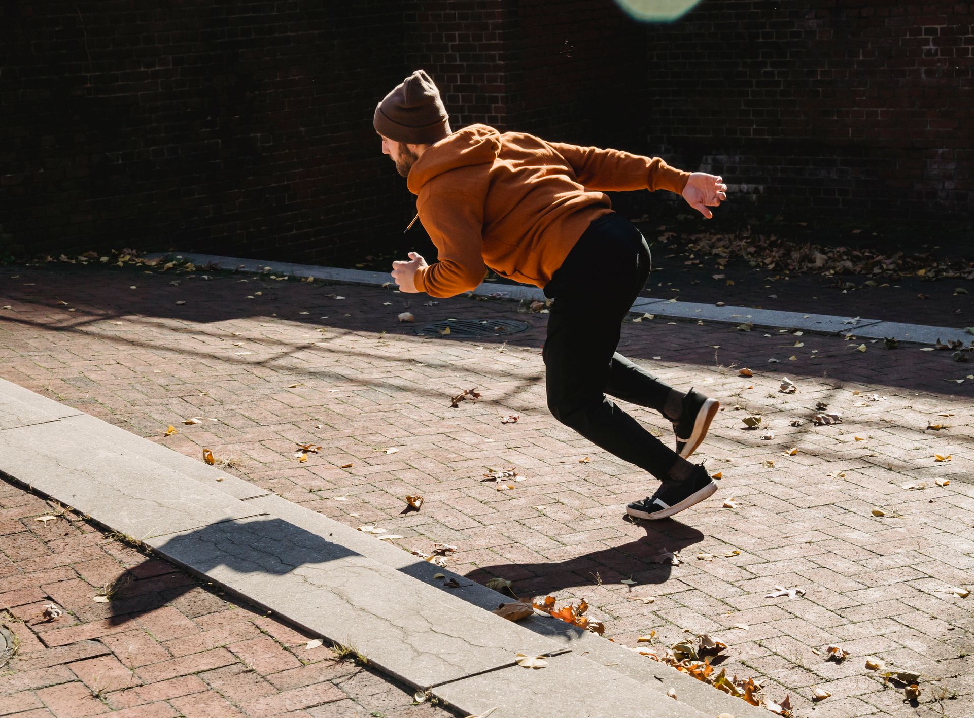 A man in casual attire performing parkour on a sunny day in an urban setting during fall.