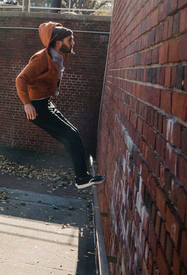 Focused Man Balancing On Metal Ledge On Brick Wall