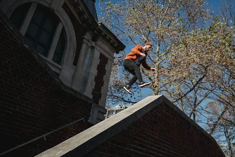 Determined Male Tracer Jumping Above Brick Building Parapet