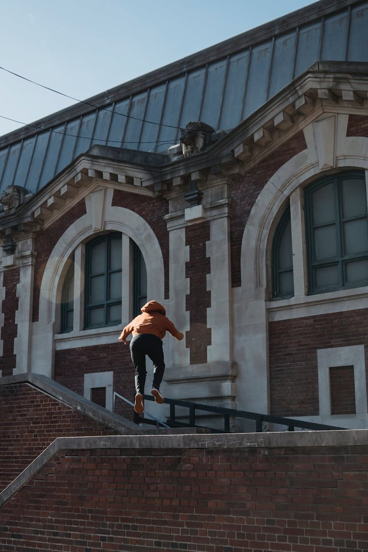 Anonymous Person Jumping Over Brick Building Parapet