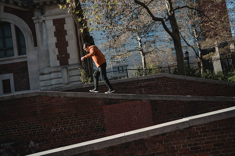 Man Walking On Brick Building Parapet