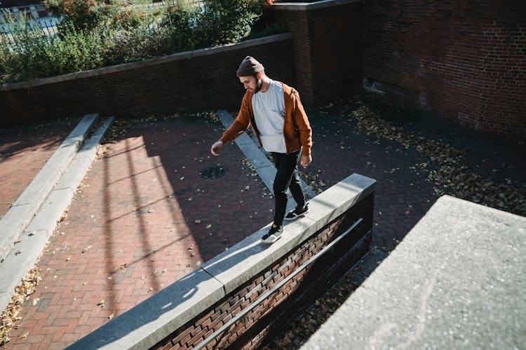 Young Man Walking On Brick Barrier Top