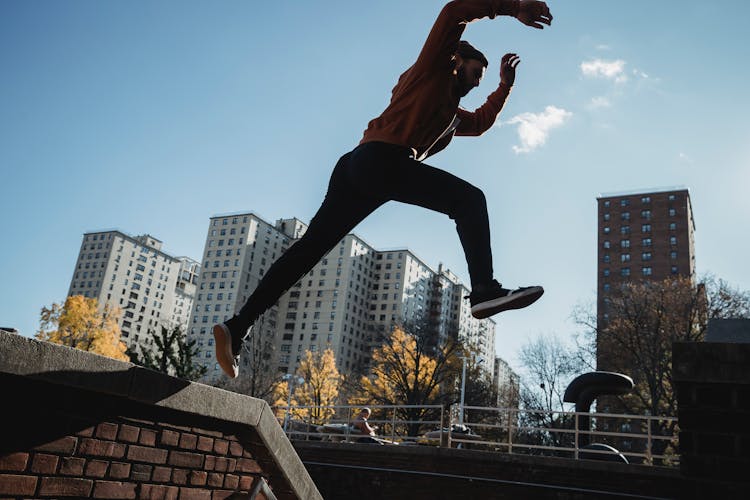 Fit Man Jumping From Brick Parapet In Urban City