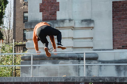 Back view full body of anonymous male athlete jumping over railing while performing parkour in city