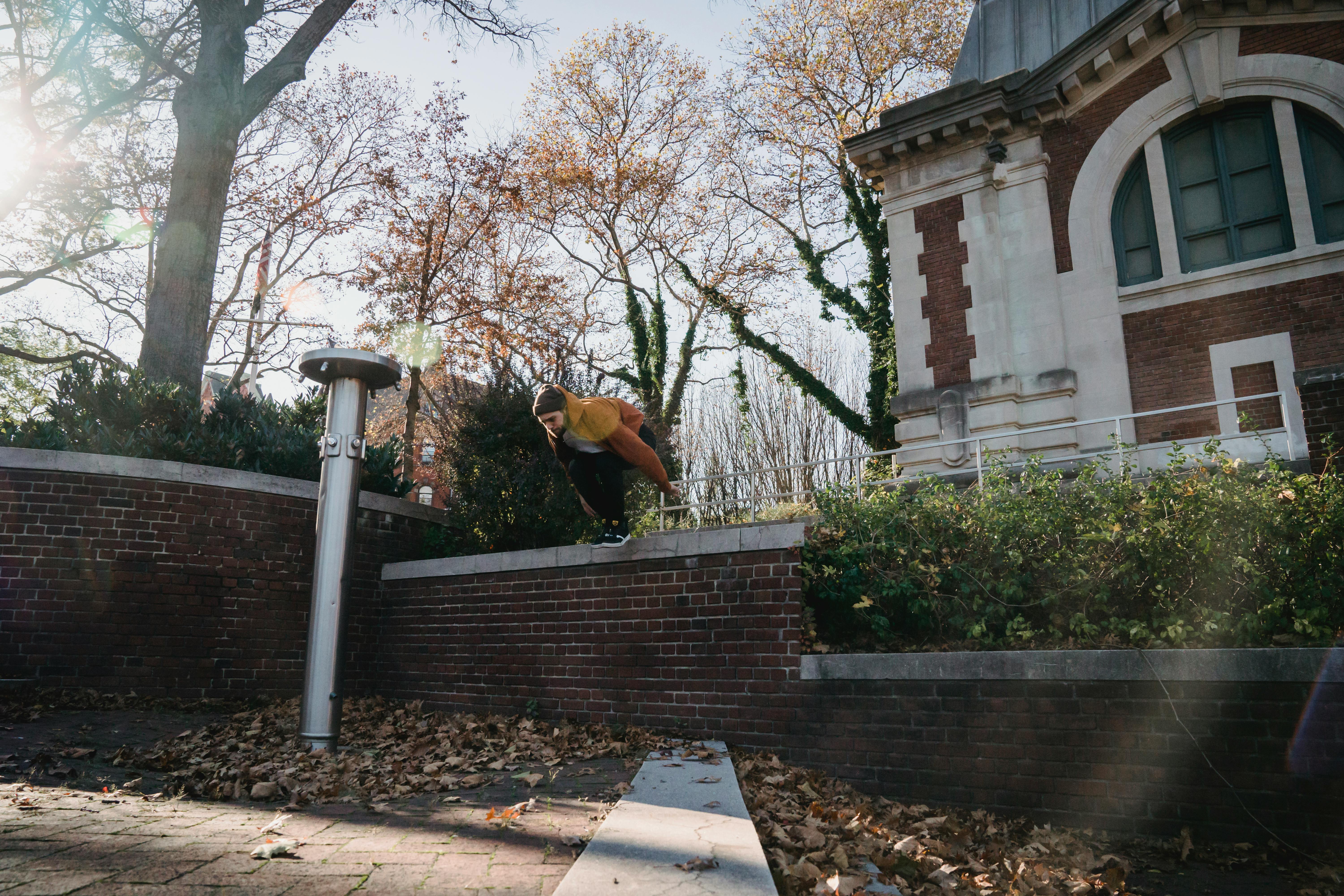 A young man performing a parkour jump over a brick wall in an urban setting during fall.